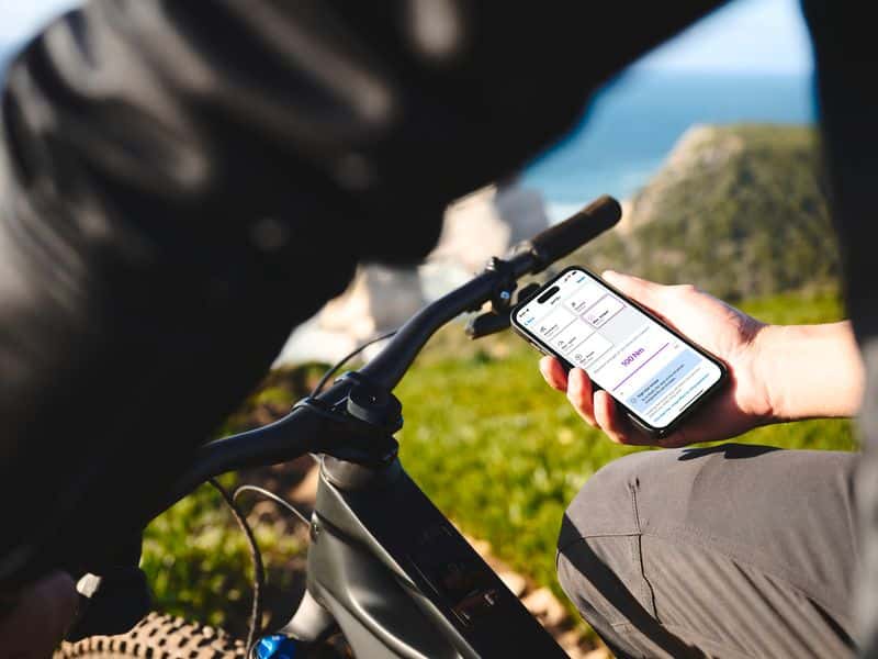 Rider checking the Bosch eBike Flow app on a smartphone next to a Bosch-powered e-MTB