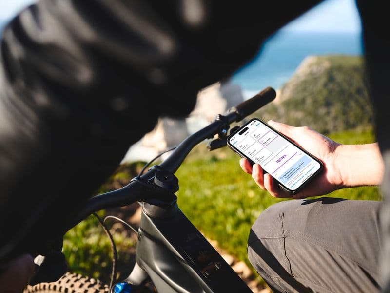 Rider checking the Bosch eBike Flow app on a smartphone next to a Bosch-powered e-MTB