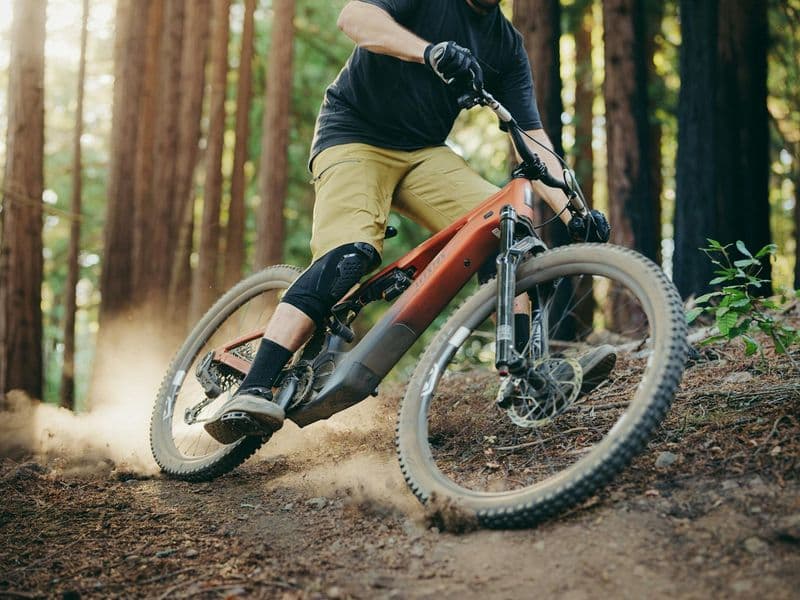 Rider cornering on a forest trail on the Aventon Current LTD eMTB in Magma orange