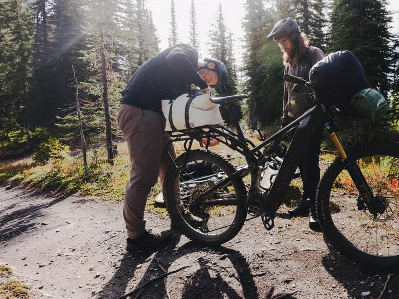 Specialized S-Works Turbo Levo 4 X loaded for an overnight trip, riders packing at a forest camp