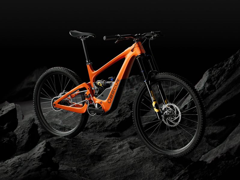Obscur Enyx e-MTB in orange on dark rocks