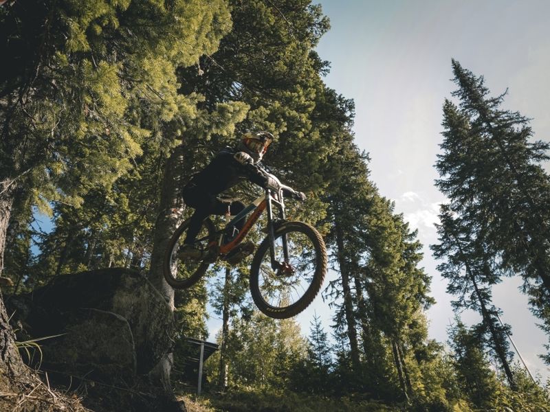 Downhill rider jumping in the forest at Sector E bike park, Sheregesh