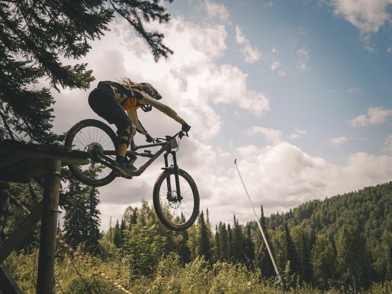 Rider dropping off a wooden kicker with taiga behind, Sheregesh