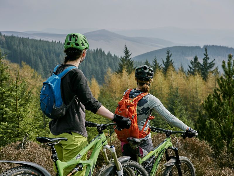 Two riders with mountain bikes at a viewpoint over Glentress forest