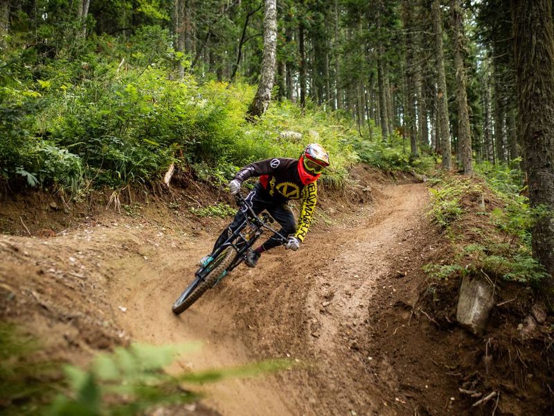 Mountain biker cornering a berm on a forest trail at Sheregesh bike park