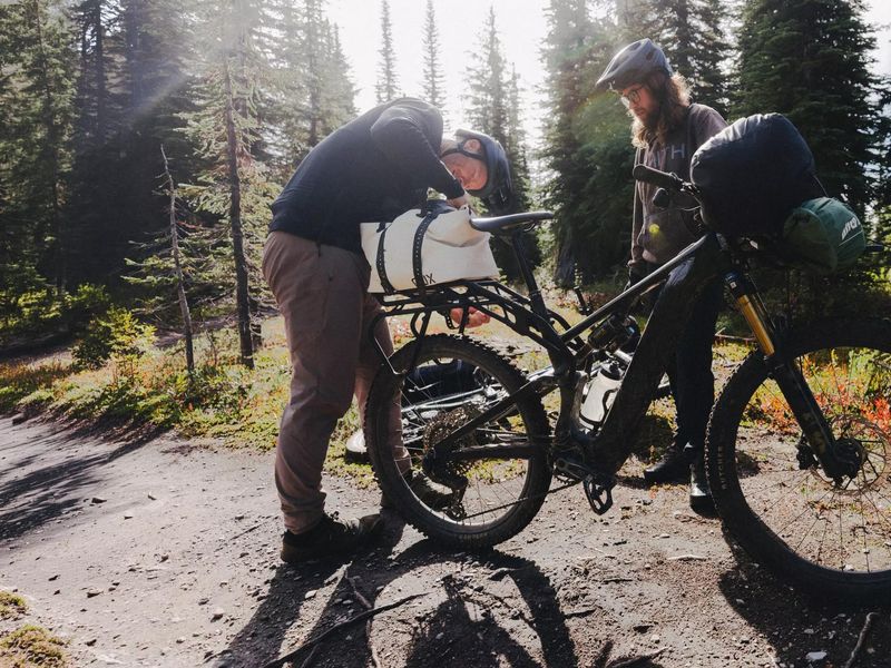 Specialized S-Works Turbo Levo 4 X loaded for an overnight trip, riders packing at a forest camp